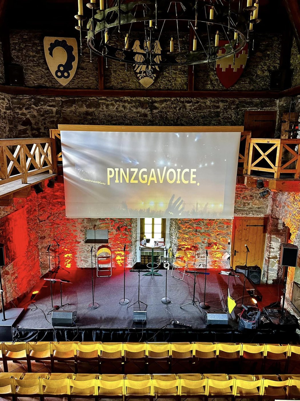 Bühne im Burgsaal, Leinwand mit PinzgaVoice, leere Stuhlreihen.